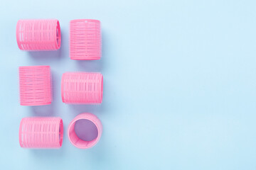 Pink hair curlers on color background, top view