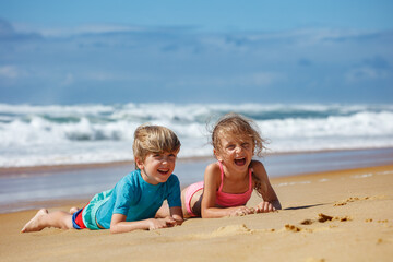 Children laughing and play at sandy beach by ocean on vacations