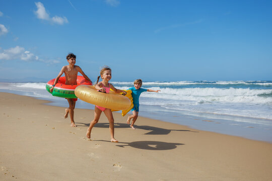 Group of kids running playing on beach with inflatable floaties