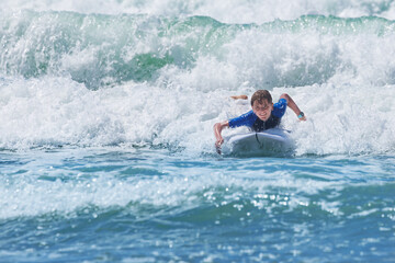 Young boy smile joyfully surfing on a wave at the sunny beach