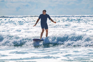 Man in wetsuit skillfully surf on a wave at bright ocean waters