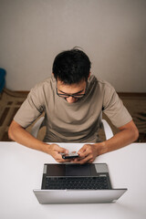 Focused bearded businessman working late at night in home office, using smartphone and laptop to manage business tasks and meet deadlines with focused concentration and professionalism
