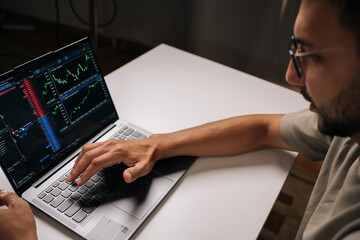 Close-up of trader in glasses typing on laptop keyboard, engaging in online trading and financial analysis, viewing real-time charts and data for informed investment decisions at home office.