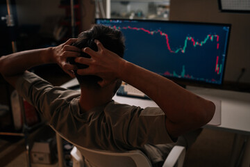 Worried trader in home office stares at red stock and crypto chart on desktop computer, showing sharp bearish downturn and causing stress, anxiety and financial concern. Concept of financial crisis.
