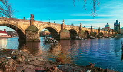 A picturesque view of Charles Bridge in Prague, Czech Republic, bathed in the warm glow of sunlight, reflecting over the Vltava River.
