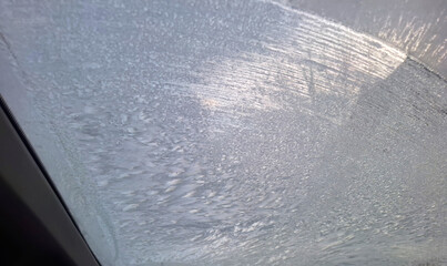 Macro photography of a car windshield covered with thick frost and ice crystals on a cold winter morning after a snowy night showing freezing weather conditions in the city area