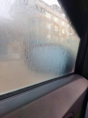 Condensation and tiny water droplets on a car side window during a cold winter day with a blurry city background showing the effect of temperature difference in the morning time