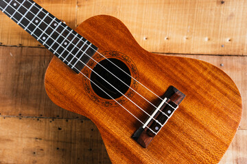 Fototapeta premium A classic brown acoustic ukulele with white wooden strings rests on a rustic wooden table like a folk musical instrument ready to play a jazz and rock music concert