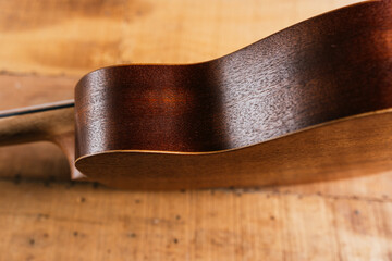 A classic brown acoustic ukulele with white wooden strings rests on a rustic wooden table like a...