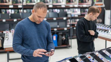 Two Caucasian men are choosing a smartphone in a store.