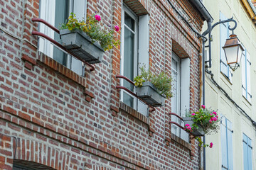 The building has three window boxes with flowers in them in France. The boxes are placed on the...
