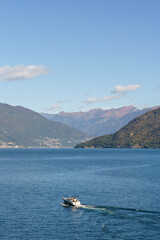Lake Maggiore in Italy with green mountains in the background The weather is clear and the water is sunny and calm A small motorboat is moving along the water