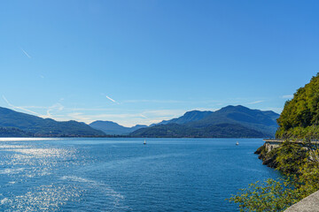 Lake Maggiore in Italy with green mountains in the background. The weather is clear and the water is sunny and calm