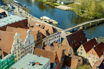 A city view with a river running through it in Lubeck Germany. The buildings are old and have red roofs. The city appears to be a mix of residential and commercial areas
