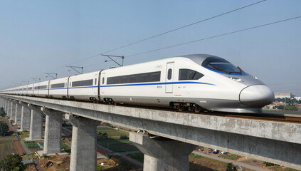 Fototapeta premium Cinematic high-speed train on a concrete viaduct slicing through a rural landscape under a clear blue sky