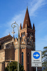 An ancient church building made of red brick with white elements in the city of Verona, Italy The sky is blue, sunny with light clouds.