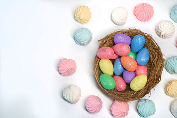 Festive Easter background. A bird&rsquo;s nest filled with glittery colored eggs surrounded by pastel meringue treats. Holiday celebration concept. Photo