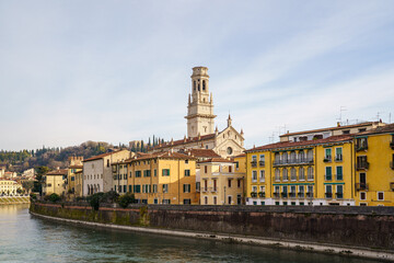 A view of part of the city on the waterfront in Verona, Italy. The tall, pointed bell tower of the church is visible