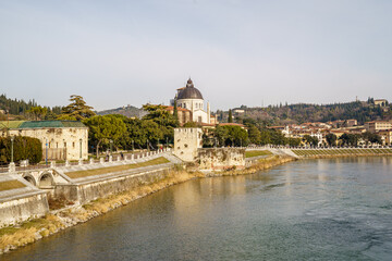 A Adige river in Verona Italy runs through a city with a large building in the background The water is calm and the sky is clear