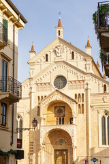 The cathedral complex in Verona, Italy. The building is made of white stone. The tower is visible on the right The sky is blue and bright.