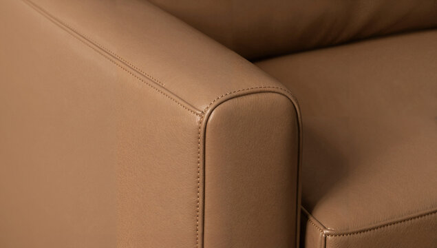 Macro close-up of a cognac leather armchair: visible natural grain, tight stitching, and curved edge detailing