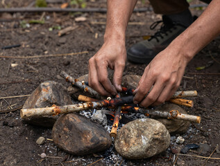 Obraz premium Hands arranging dry sticks around a small campfire inside a stone ring on dirt in a forest
