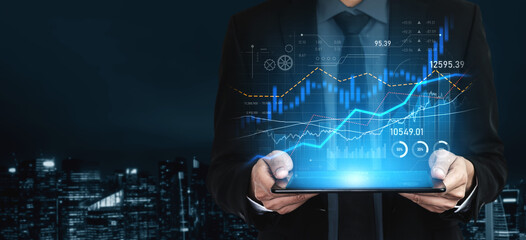A business professional stands in an urban setting at night, analyzing financial data trends displayed on a tablet with vibrant stock market graphs and indicators. Scalp