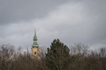 An old metal church tower with a clock, its upper part rising above the forest.
