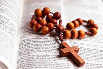 Simple wooden rosary beads with a crucifix on an open Bible representing spirituality and devotion
