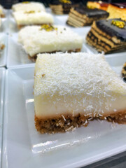 A slice of delicious traditional milky dessert with semolina and coconut sprinkles served on a white plate in a cafe for people who enjoy light and sweet mediterranean treats today now