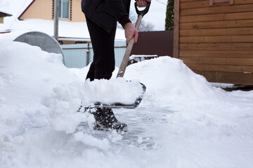 Individual shoveling snow from a driveway with a metal shovel, surrounded by a winter landscape,...