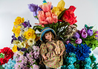 young girl doll with glass eyes sitting in front of spring flowers with white background