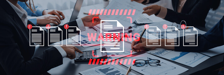 Business team actively engages in data analysis and document review in a modern office setting, amidst digital warning signs and collaborative discussions. Gantry