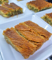 Delicious traditional Turkish kadayif dessert with crispy shredded wheat and pistachio filling served on a white plate in a restaurant with a golden brown crust and sweet sugar syrup