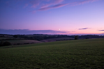 Sunset dusk landscape in the beautiful green hills of the Cotswolds in England with the moonlight