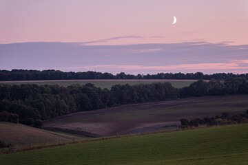 Sunset dusk landscape in the beautiful green hills of the Cotswolds in England with the moonlight