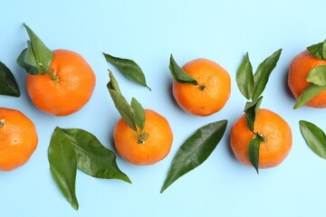 Fresh juicy tangerines and green leaves on light blue background, flat lay