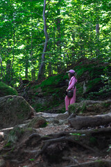 Girl in pink outfit exploring a lush green forest with rocky terrain