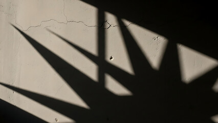 Dramatic sharp-edged shadows cast by an unseen object create an abstract geometric pattern on a cracked, sunlit wall, highlighting texture and high contrast in a minimalist composition