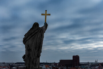 Wrocław; rzeźba z krzyżem i kościół na tle zachmurzonego nieba 