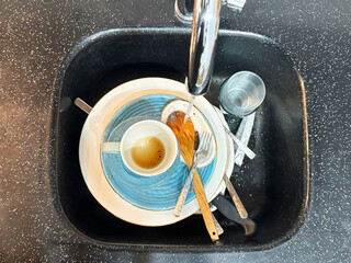 Top view of dirty dishes in sink. Overhead view of dirty dishes, cup and cutlery in black kitchen...