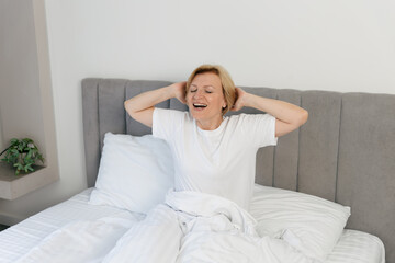 Mature woman enjoys a cozy morning in a comfortable hotel bedroom