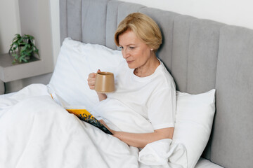 Cozy morning routine in a hotel bedroom with a mature woman enjoying a book