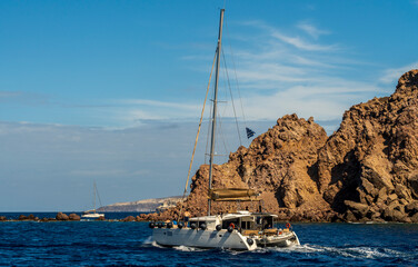 Sailboat anchored near rocky island coastline in deep blue sea
