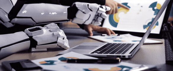 A futuristic workspace showcasing a human collaborating with a robotic arm, analyzing digital designs and creative concepts on a laptop, emphasizing innovation and teamwork.Noogenesis