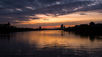 The river mirrors the city&rsquo;s silhouette in calm twilght hues