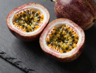 Close-up of halved passion fruits with bright yellow pulp and black seeds on a dark slate surface under dramatic lighting