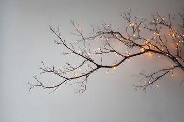 Obraz premium A bare branch adorned with warm fairy lights against a neutral wall