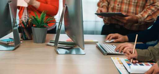 A dynamic office scene showing diverse professionals collaborating on design projects. The image captures hands actively engaging with technology and materials. SACTR