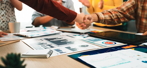 A successful meeting atmosphere captures business professionals shaking hands over financial...